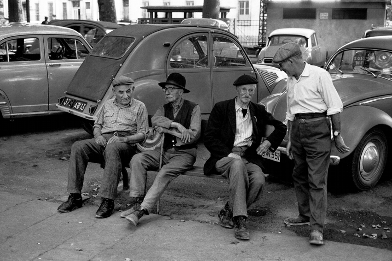 Quatre hommes âgés discutent dans un parking dans les années 60